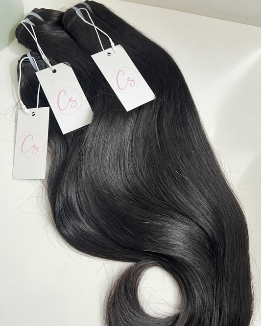 Three bundles of long, wavy black hair extensions with white tags.