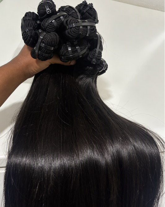 A hand holding a bundle of long, straight black Raw virgin hair extensions against a plain light background.